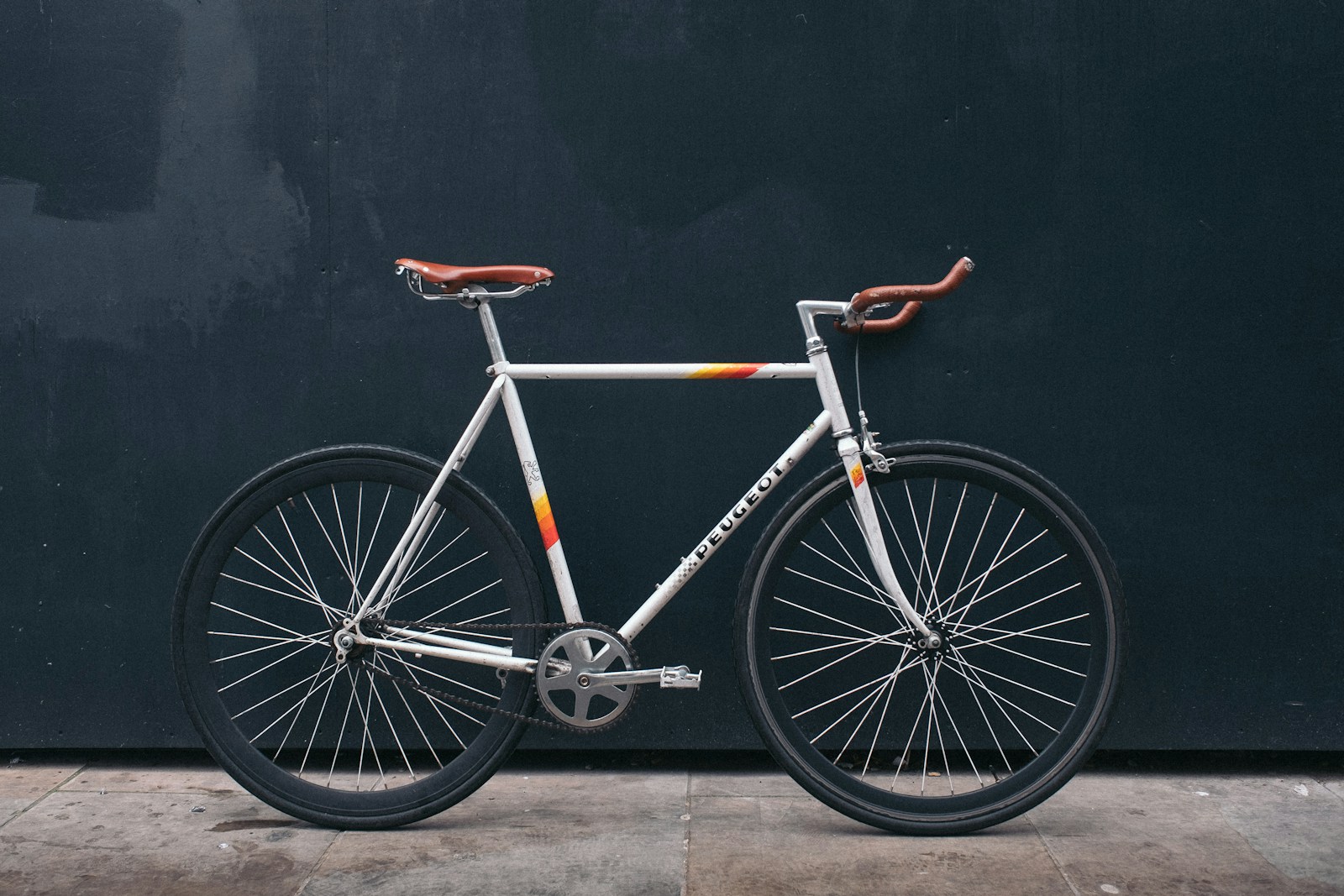 White bicycle with brown handlebars parked against a dark wall