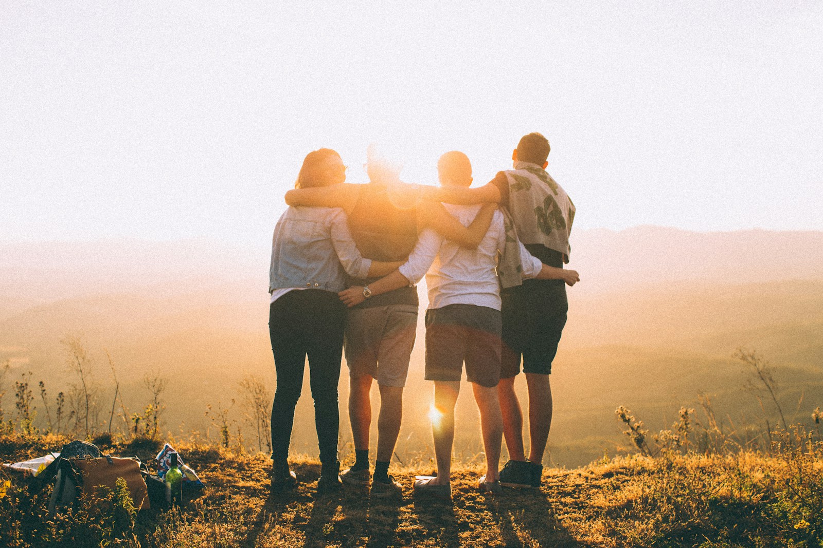Four people standing with arms around one another at sunset